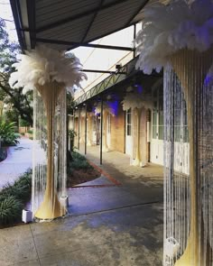 some white feathers hanging from poles on the side of a building in front of a sidewalk