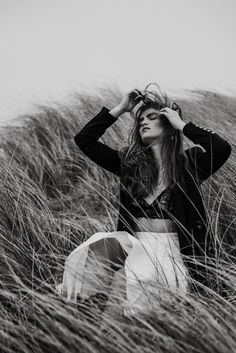 a woman sitting in tall grass with her hands on her head