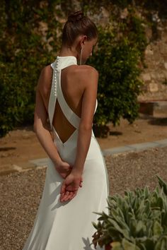 a woman in a white dress standing next to a pineapple plant and looking at the back of her dress