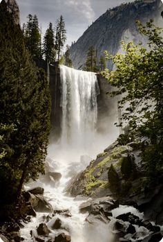 a waterfall with water flowing down it surrounded by rocks and trees in the foreground