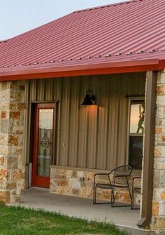 a small brick building with a red roof and two chairs on the front porch area