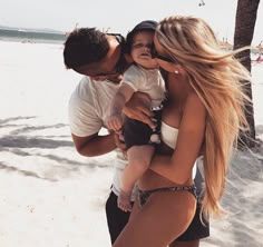 a man kissing a woman on the beach while holding a baby