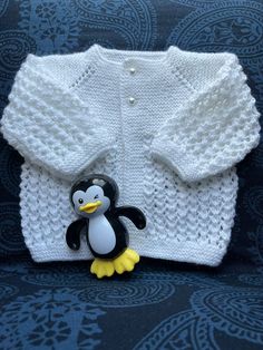 a knitted sweater with a penguin brooch attached to the front, sitting on a couch