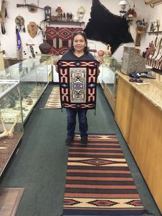 a woman holding up a blanket in a room filled with rugs and other items