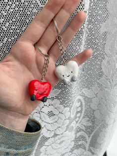 a hand holding two small red and white hearts in it's palm, with the other heart shaped keychain attached