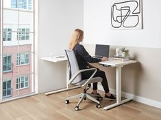 a woman sitting at a desk with a laptop on her lap and looking out the window