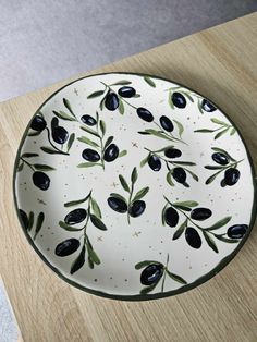 an olive plate is sitting on a wooden table top with green leaves and black olives