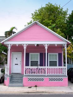 a pink house with white trim and purple shutters on the front porch is shown