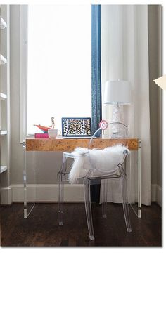 a white chair sitting in front of a window next to a desk with a lamp on it