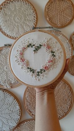 someone is holding up a hand embroidered heart on some doily with flowers in the middle