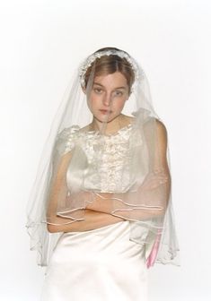 a woman in a wedding dress and veil posing for the camera with her arms crossed