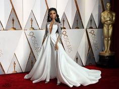 a woman in a white gown standing on a red carpet with an oscar statue behind her