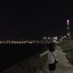 a woman is walking down a path near the water at night with her arms outstretched