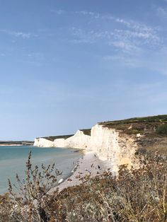 people are walking on the beach near white cliffs and blue water with clear skies in the background