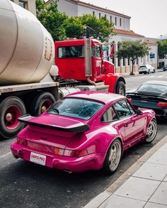 a pink car parked on the side of the road next to a red truck and cement mixer