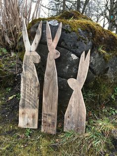 three wooden rabbits standing in front of a rock and moss covered ground with trees behind them