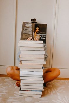 a person sitting on the floor with a stack of books in front of their face