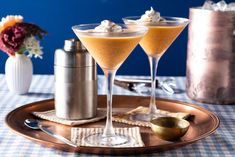 two martini glasses sitting on top of a metal tray next to a shaker and cup