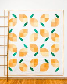 an orange and green patchwork quilt hanging on a wall next to a wooden ladder