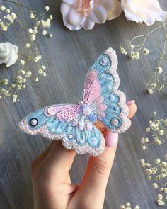 a hand holding a small blue and pink butterfly on top of a wooden table next to flowers