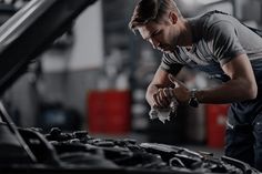 a mechanic working on the hood of a car in a garage with his hand over the engine