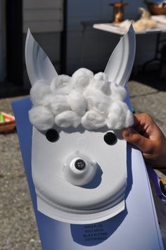 a person is holding up a fake unicorn head with white fluffy balls on it's face