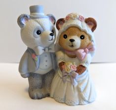 two teddy bears dressed in wedding attire standing next to each other on a white surface