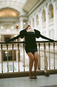 a woman standing on a balcony with her arms behind her head and looking up at the ceiling