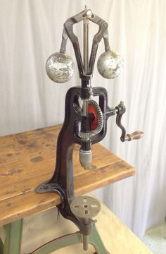 an old sewing machine with three balls on it's head and two hands, sitting on top of a wooden table