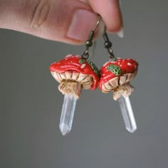 a hand holding two tiny red mushrooms on clear acrylic hooks with green accents