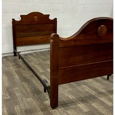 a wooden bed frame sitting on top of a hard wood floor next to a white brick wall