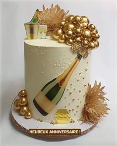 a white cake decorated with gold decorations and a bottle of champagne on the top tier