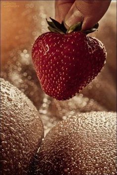 a strawberry being held up by someone's hand with water droplets around it and on top of them