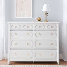 a white dresser with gold handles and knobs in a blue room next to a window