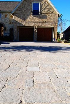 a large brick driveway in front of a house with two garage doors on each side