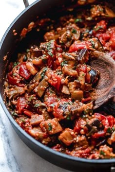 a pan filled with meat and vegetables on top of a counter next to a wooden spoon