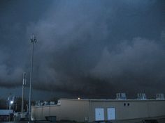 dark clouds loom over an industrial building and parking lot in the distance at night