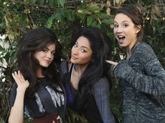 three young women posing for the camera in front of some trees and bushes with their mouths open