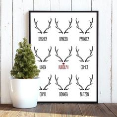 a poster with reindeer antlers on it next to a potted plant in front of a white wall