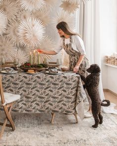 a woman standing at a table with a cake on it next to a dog and another person