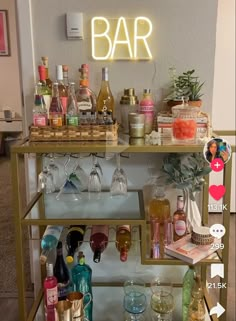 a bar cart filled with lots of bottles and glasses next to a neon sign that says bar