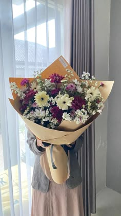 a woman holding a bouquet of flowers in front of a window with sheer drapes