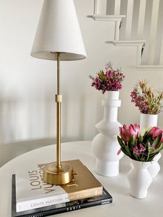 three vases with flowers are sitting on a table next to a book and lamp