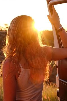 a woman standing in front of a truck with the sun shining through her hair and holding onto the door handle