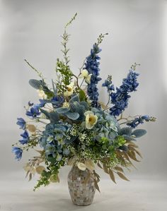 a vase filled with lots of blue flowers and greenery next to a white wall