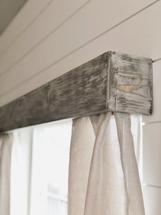 an old window frame is hanging on the side of a white house with sheer curtains