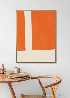 an orange and white painting hangs on the wall next to a table with two chairs