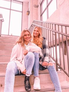 two young women sitting on the steps in front of a building smiling at the camera