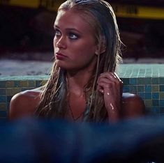 a woman with long hair sitting in a bathtub next to a tiled wall and looking off into the distance