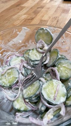 a glass bowl filled with cucumbers and onions on top of a wooden table